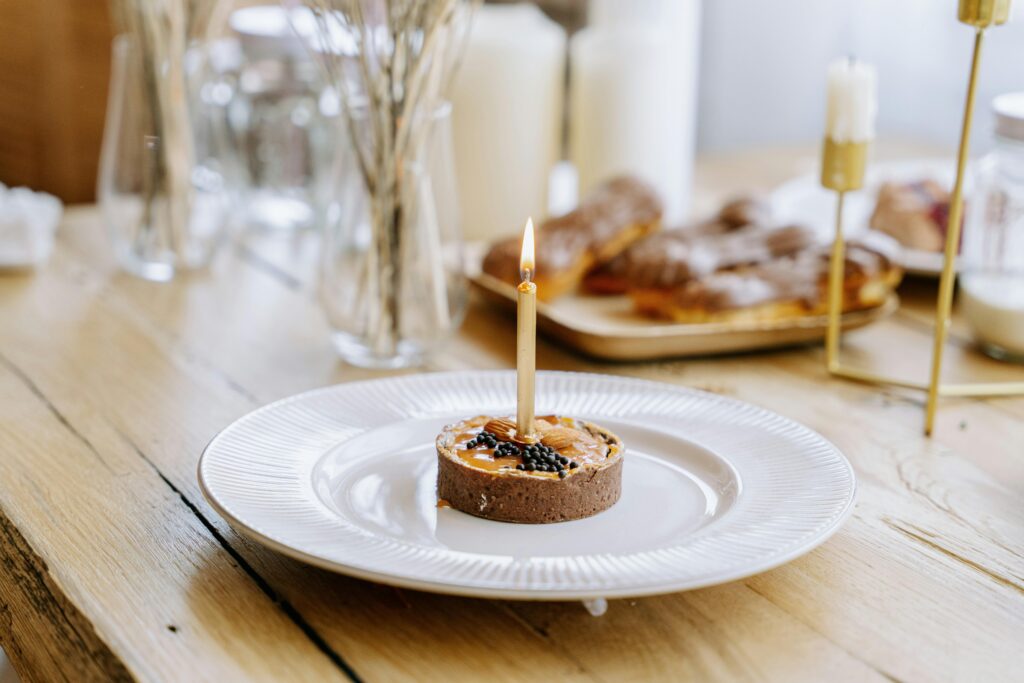 Dessert tart with candle on porcelain plate with eclairs in the background