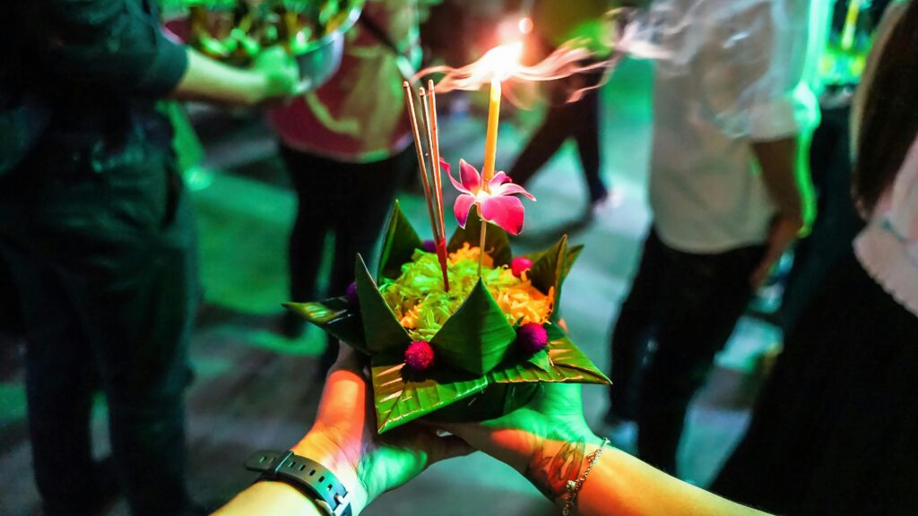 Banana leaf basket decorated with flowers, incense, and a lit candle floating on water during Thailand’s Loy Krathong festival, symbolizing renewal and letting go of negativity.